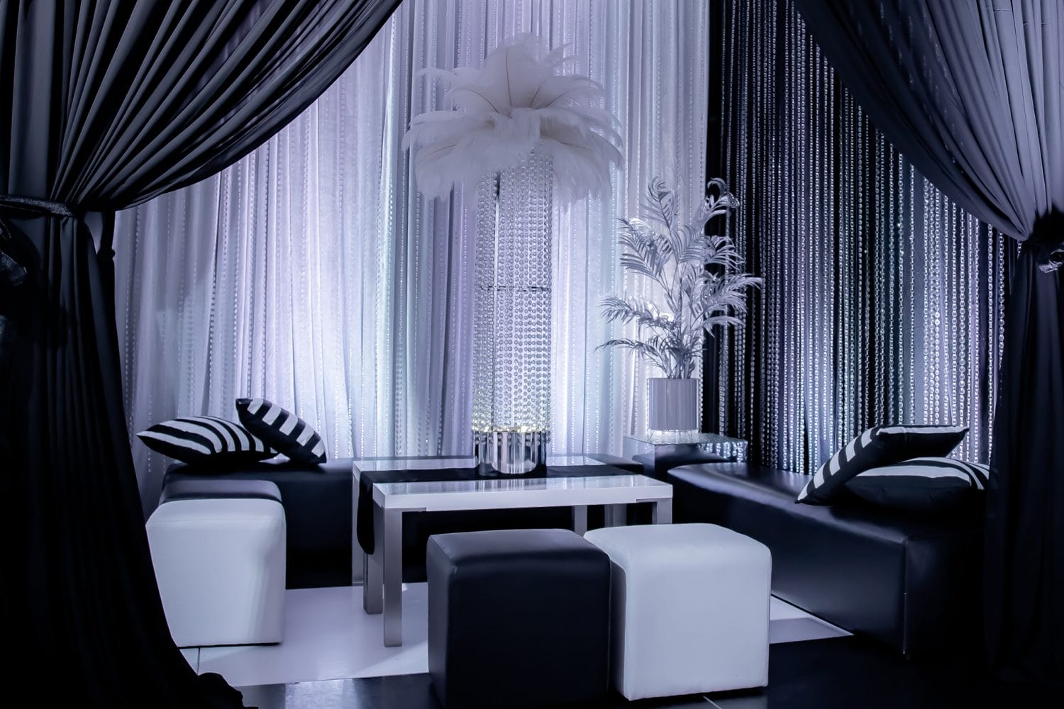 luxurious seating area at black & white party. Features chiffon drape, ottomans, and a feather centrepiece