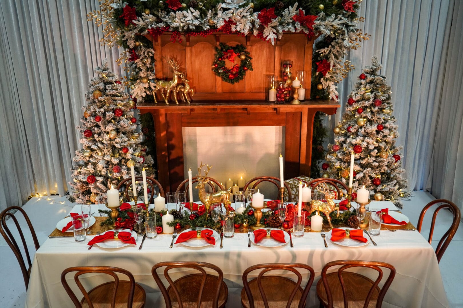 christmas themed dinner table setup with themed decor and a christmas mantlepiece and christmas trees