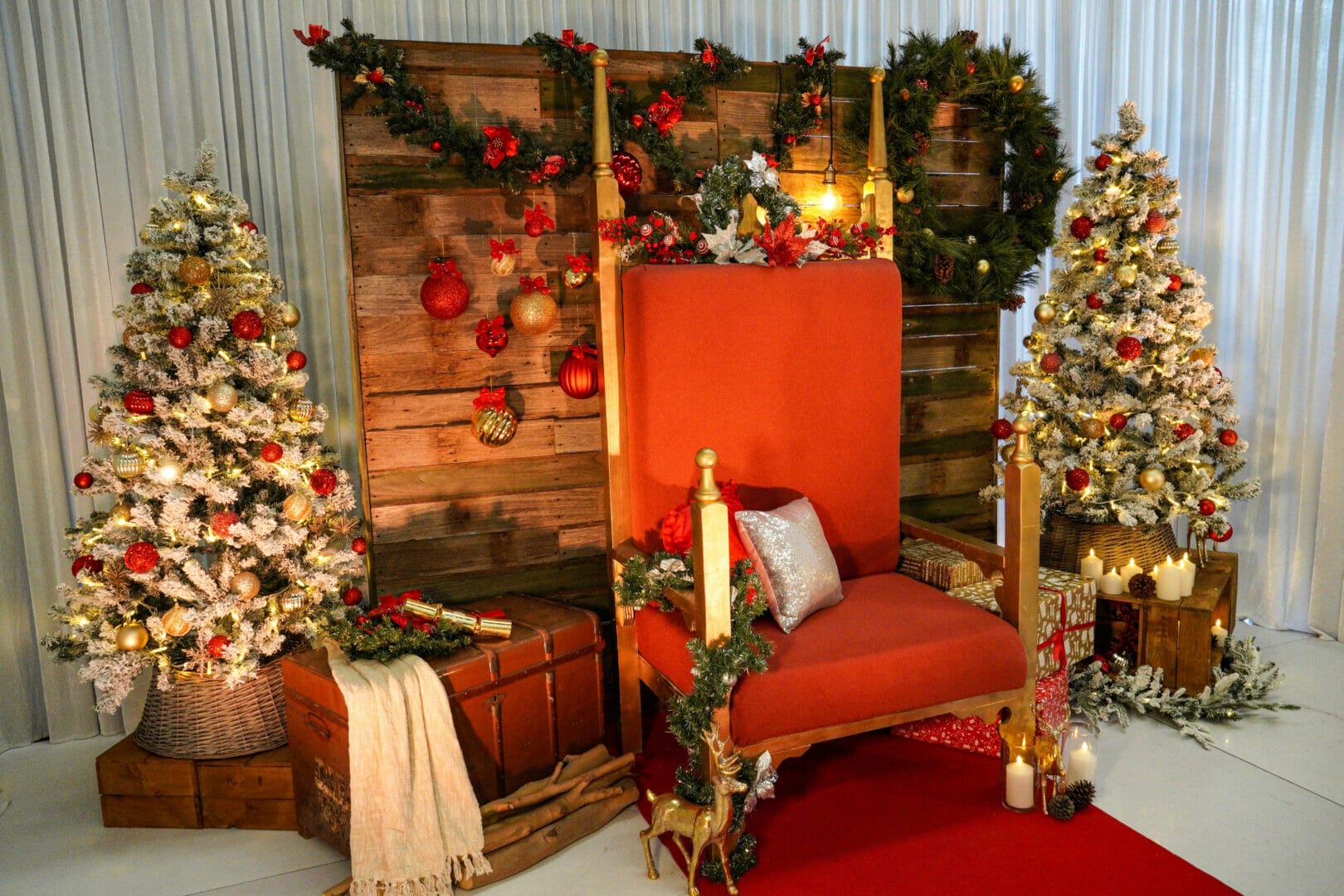 christmas themed backdrop with a santa throne, christmas trees, ornaments, garlands, wreaths, presents, and a rustic backdrop