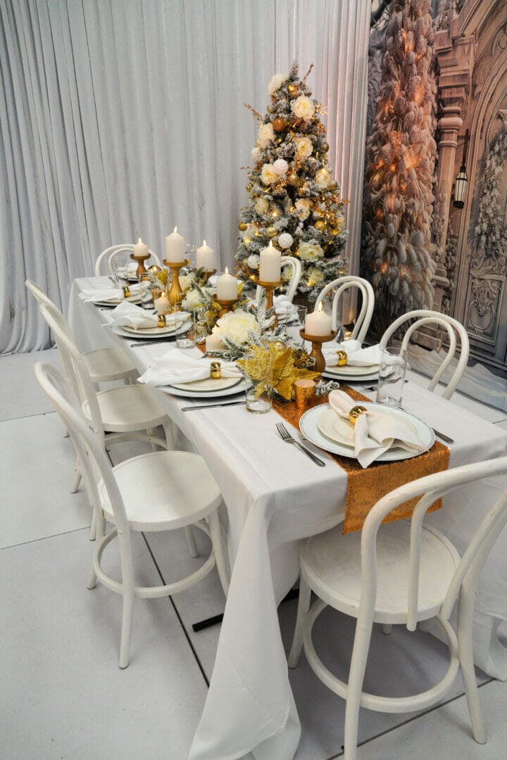 Christmas themed dinner party setup with white and gold themed table decor, themed backdrop, and christmas trees