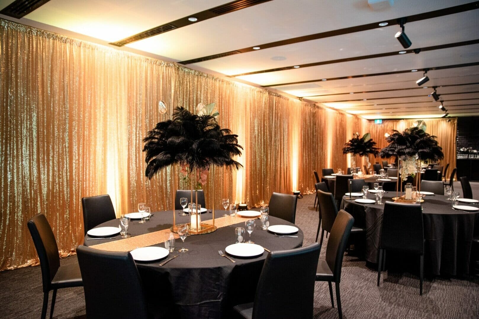 Gold sequin drape, black feather centerpieces, and table setups at puffing bill event space setup