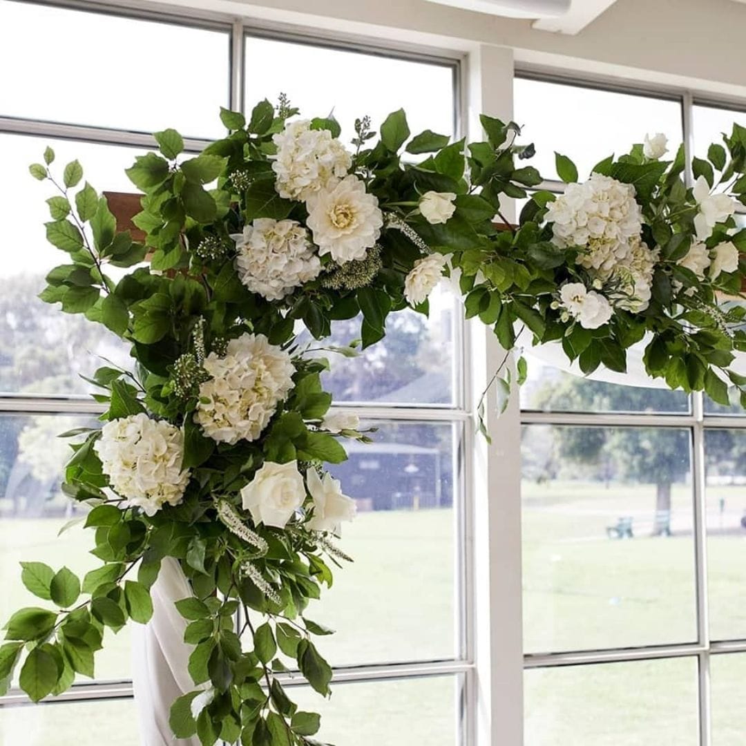 white floral arrangement on wedding arch with fresh greenery by juliet louise