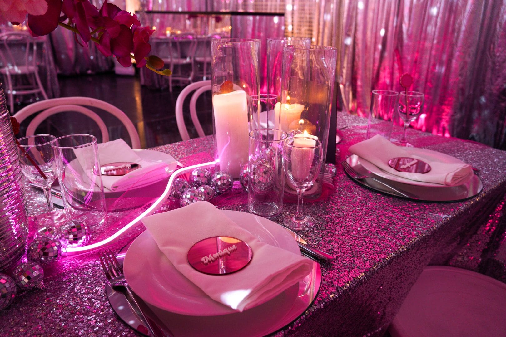 Pink disco dinner party table setup. Featuring custom signage, silver sequin table overlay, and various pink and silver styling items