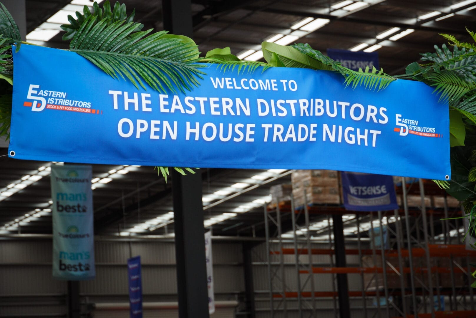 Blue and White entrance banner to Eastern Distributors Open Trade Night with greenery around it