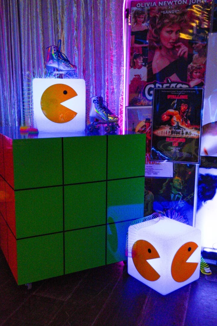 LED Cube with Pacman acrylic on it surrounded by slinkys and roller skates sitting on a large Rubik's cube at 80s themed partyLED Cube with Pacman acrylic on it surrounded by slinkys and roller skates sitting on a large Rubik's cube at 80s themed party