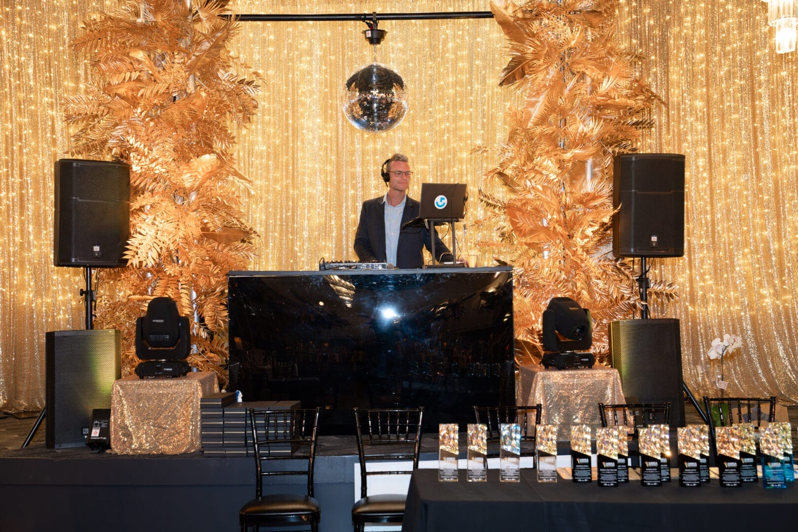 DJ booth with gold leaf and floral installation and gold drape and fairy light backdrop