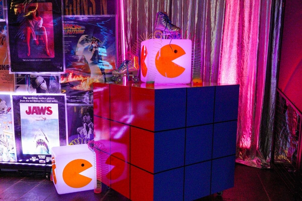 LED Cube with Pacman acrylic on it surrounded by slinkys and roller skates sitting on a large Rubik's cube at 80s themed party