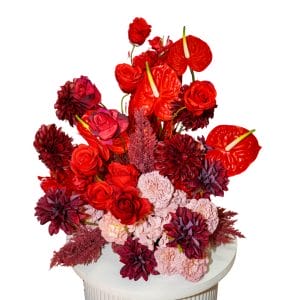 Red and dusty pink floral arrangement sitting on a white ripple plinth
